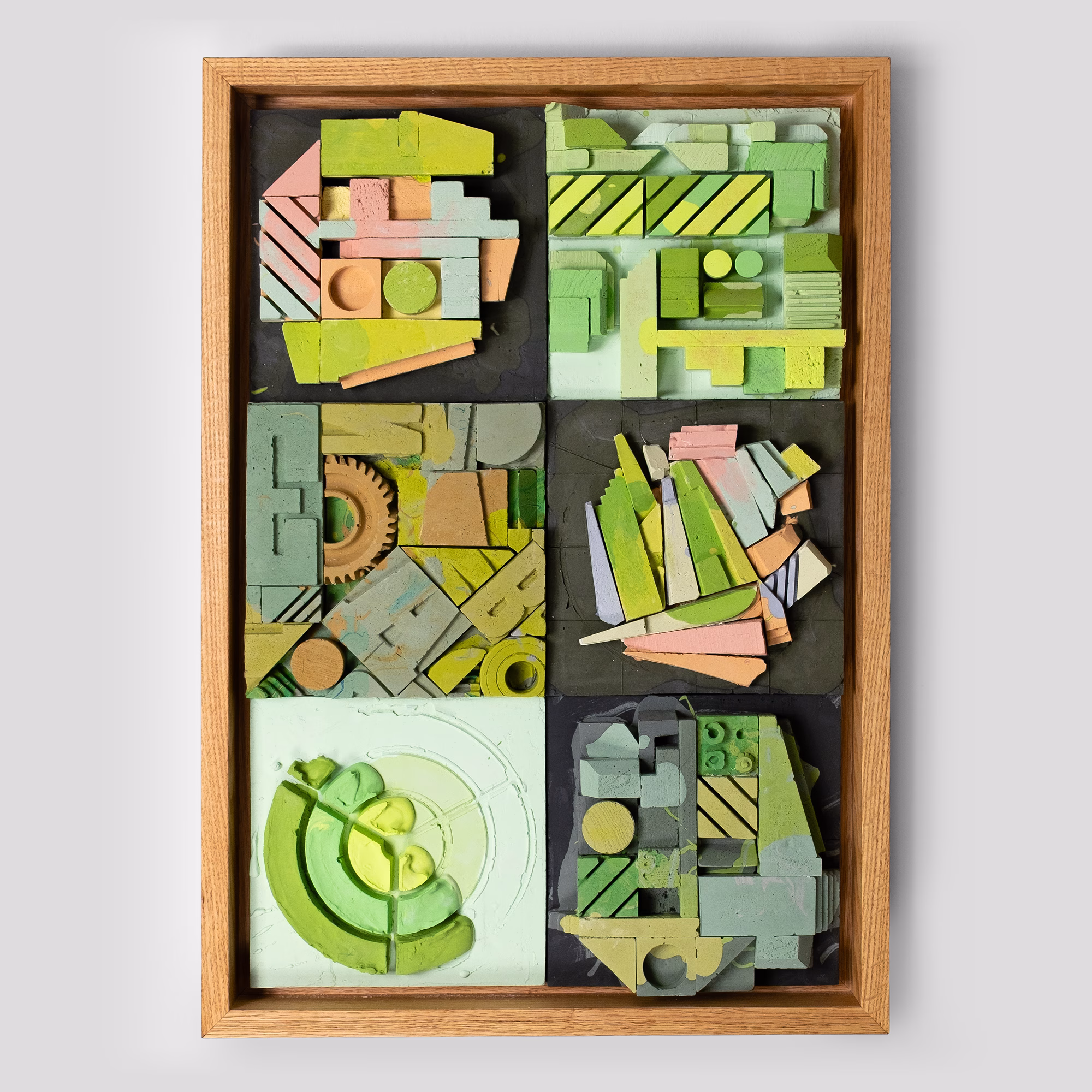 A front-on photograph of a framed, 3D mixed-media relief sculpture. The piece is composed of six distinct, colorful panels arranged in two columns. The colors are predominantly pastel, featuring mint green, lime, terracotta, pale pink, lavender, and black. Various shapes like gears, letterforms, and geometric blocks create a complex, textured archaeology within a natural wood float frame.
